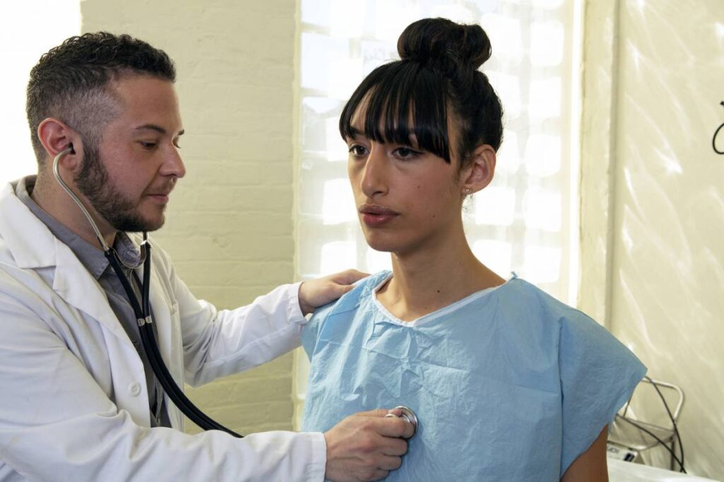 a_transgender_woman_in_a_hospital_gown_being_treated_by_a_doctor_a_transgender_man