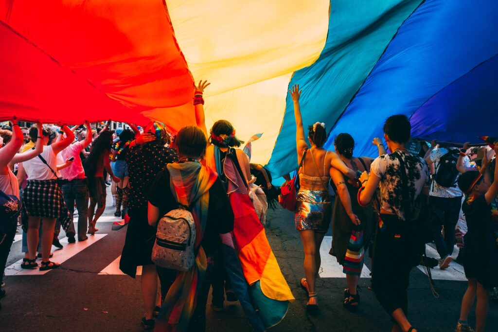 Pride Parade goers march under a giant pride flag