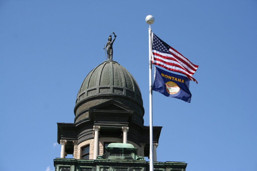 American and Montana state flags fly in front of Montana courthouse.