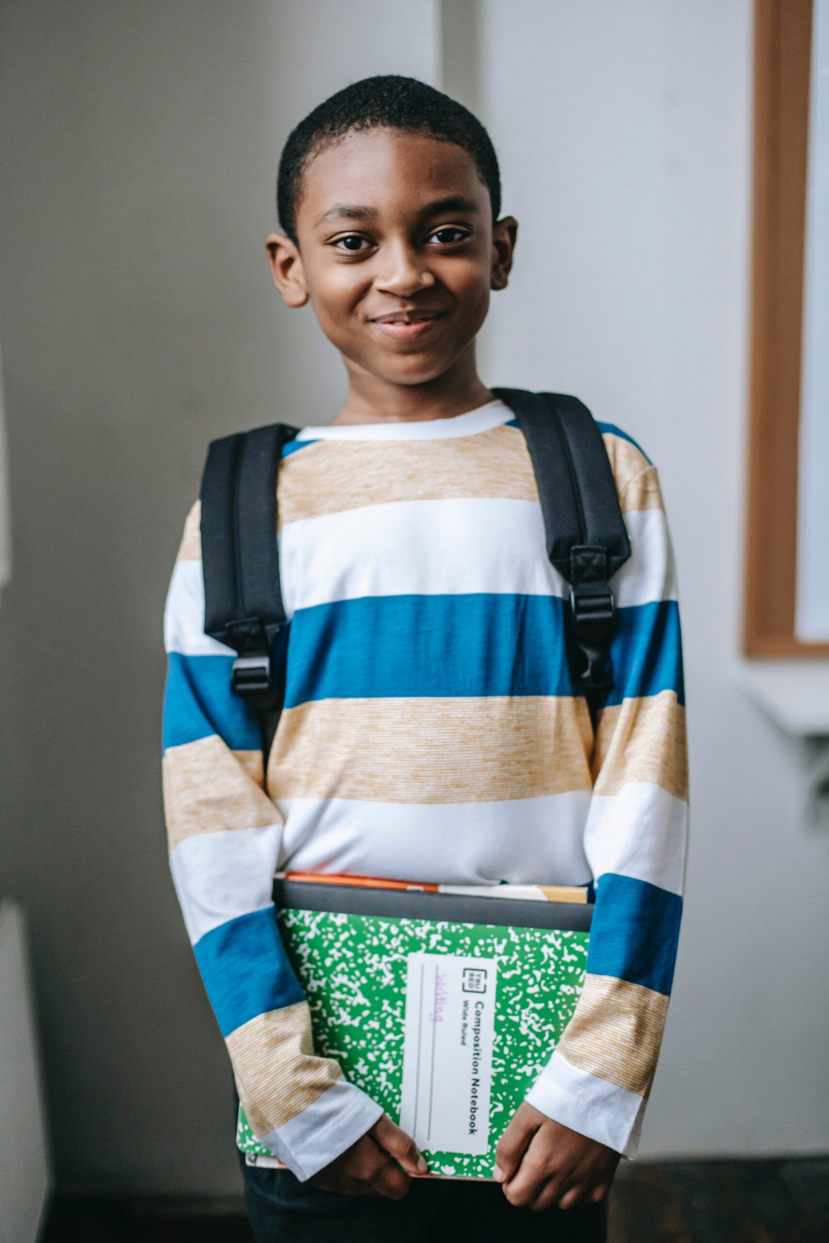 young boy smiling wearing backpack and holding notebook
