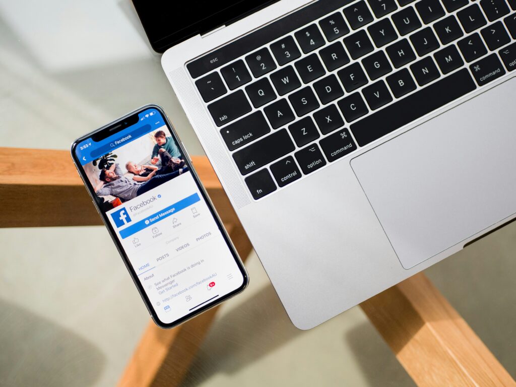 A smartphone is open to Facebook on a table next to a laptop.