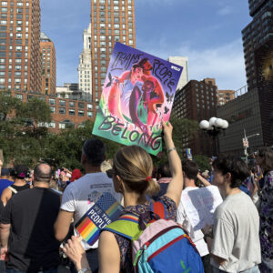 Person facing away from camera holding a sign that reads "trans people belong"