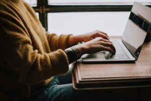 person in yellow sweater with bracelets typing on a laptop at a desk